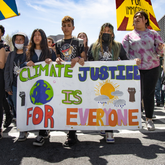 A group of young protesters hold a banner at an action outside that reads "Climate justice is for everyone."