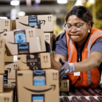 A Black woman warehouse worker moves Amazon boxes on a conveyor belt