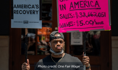 A Black man holds two signs that read: "Low Wages Stop America's Recovery", and "Old Ebbit Grill #5th highest grossing eatery in America. Sales: $32,662,051 Wages: $5.00/hour". photo credit: One Fair Wage