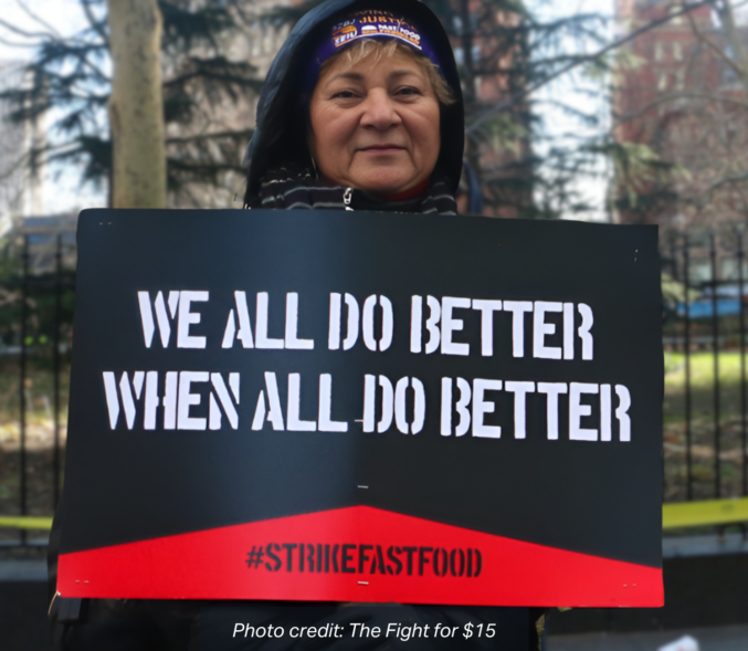 A white woman wearing a parka holds a sign that reads: "We All Do Better When We All Do Better, #StrikeFastFood". This image has been altered from its original format using AI. photo credit: The Fight for $15