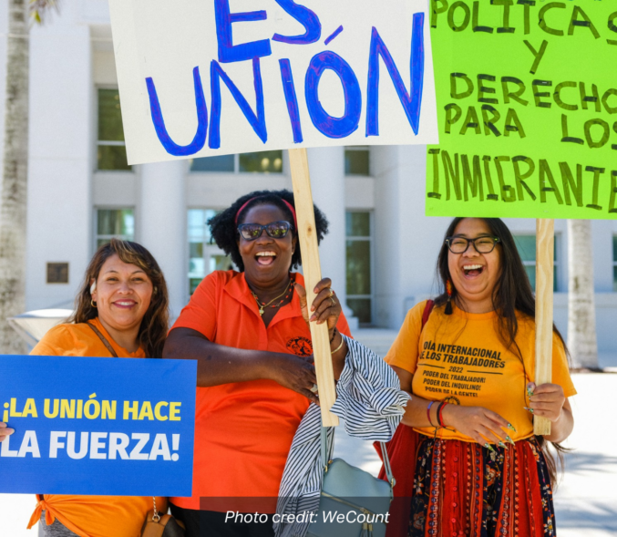 A trio of smiling Women of Color carry signs that read: "La Union Hace La Fuerza! and Politicas y Derechos Para Los Immigrantes". photo credit: We Count