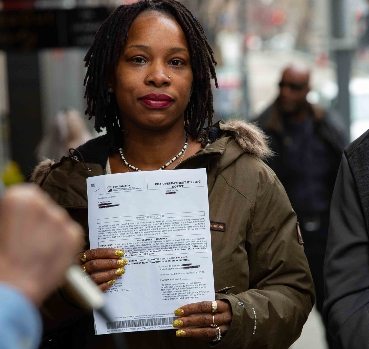 A portrait of a Black woman holding a pandemic unemployment assistance overpayment notice.