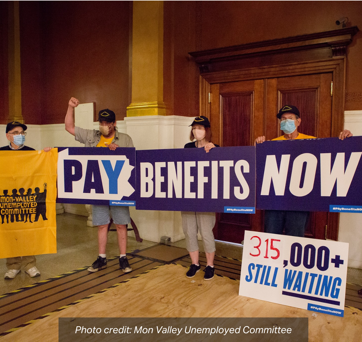 A group of advocates hold up a sign in front of the Governor's Office that reads: "Pay Benefits Now, 315,000+ Still Waiting". photo credit: Mon Valley Unemployed Committee