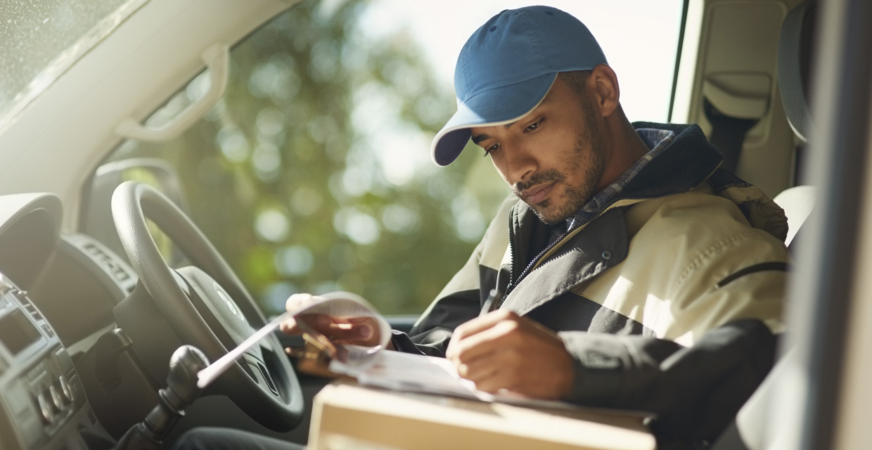 A delivery man reads addresses while sitting in a delivery van.