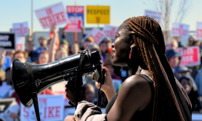 An African American woman speaking into a bullhorn before a crowd of striking workers.