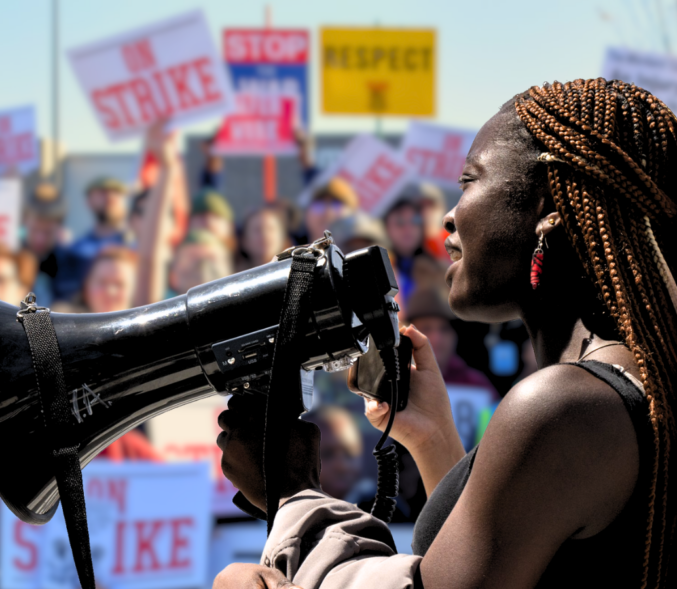 An African American woman speaking into a bullhorn before a crowd of striking workers.